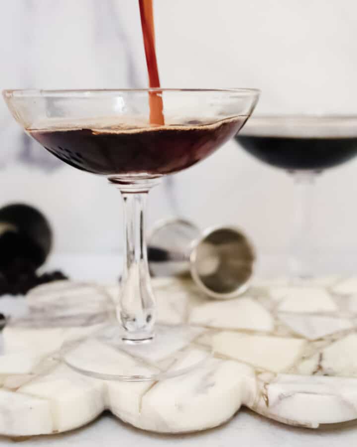 Espresso Martini being poured in a coupe glass with fresh coffee beans