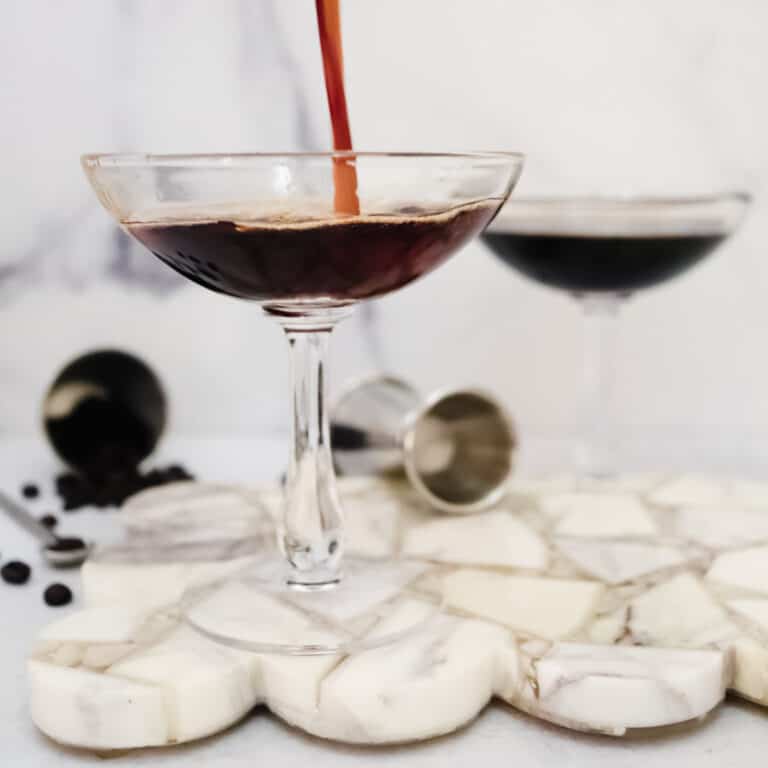 Espresso Martini being poured in a coupe glass with fresh coffee beans