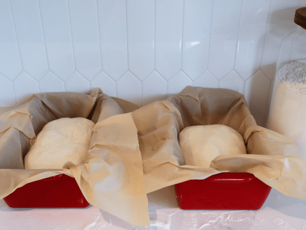 Loaves sitting over parchment paper in red bread loaf pans