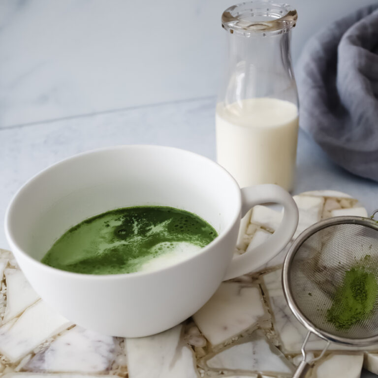 Rishi Tea Barista Matcha powder, almond milk, and honey arranged on a marble surface for an easy matcha latte recipe