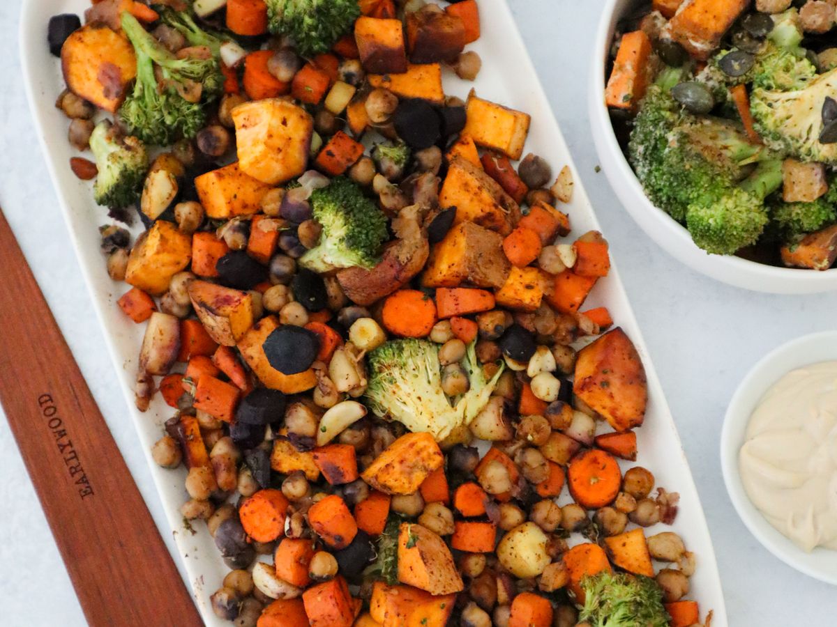 Platter of roasted rainbow carrots, broccoli, sweet potato, and chickpeas with a bowl of tahini dressing alongside