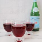 Sparkling blueberry iced tea in footed glasses with a bottle of sparkling water