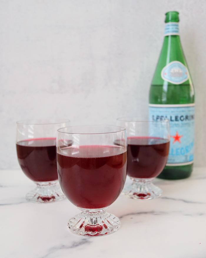 Sparkling blueberry iced tea in footed glasses with a bottle of sparkling water